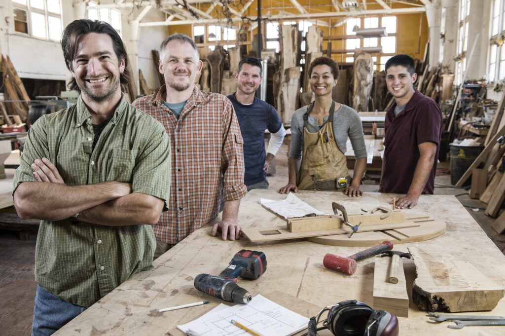 Team of multi-racial factory workers standing next to a work station in a large wood working